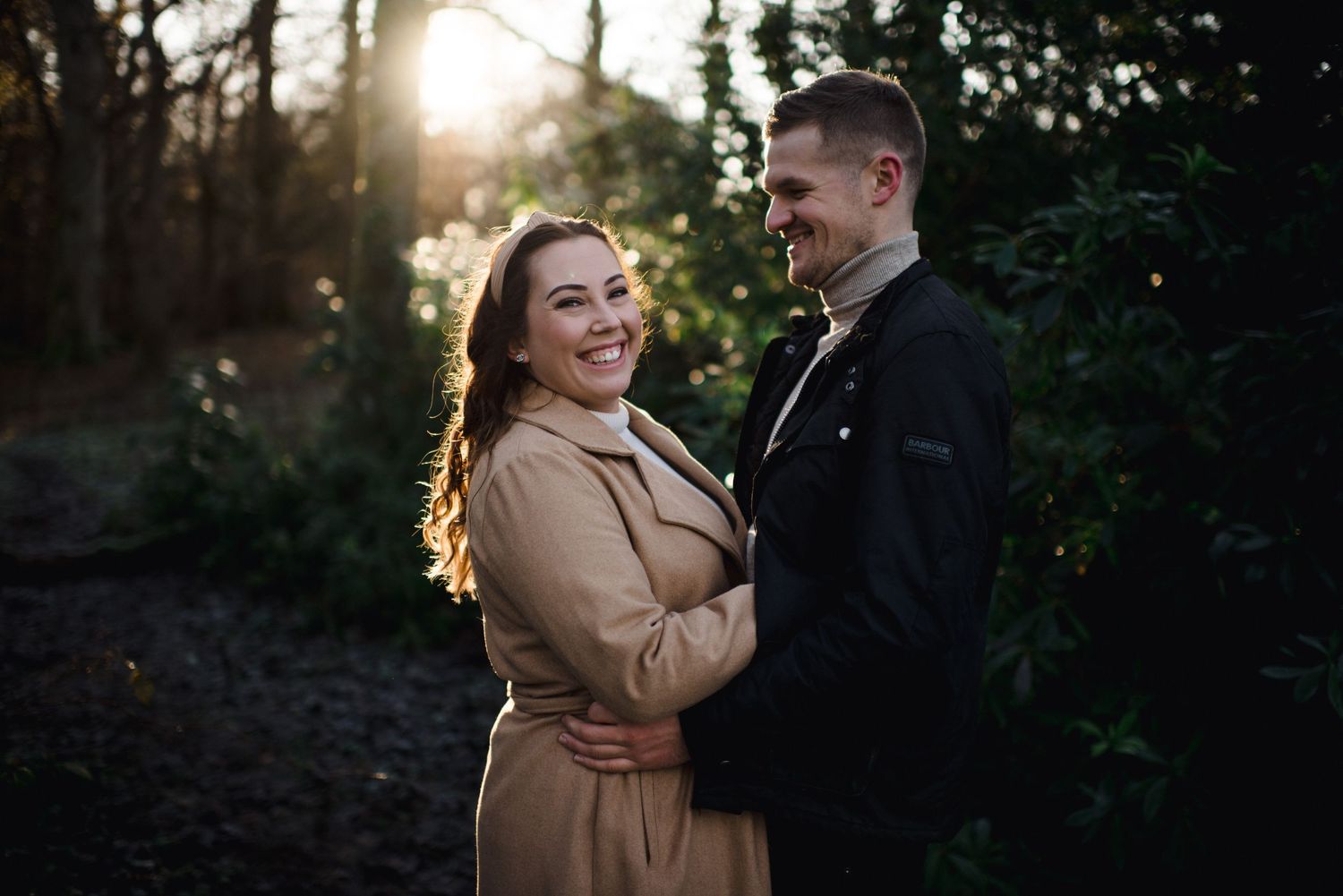 A joyful couple laughs together during their sunset engagement session in the woods.