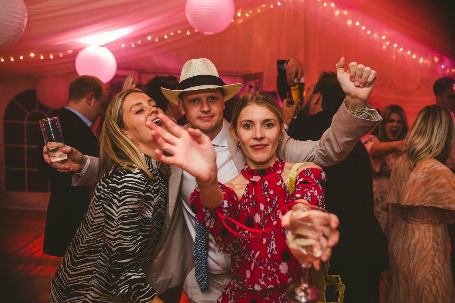 Wedding guests dancing and celebrating in a festively lit red tent.