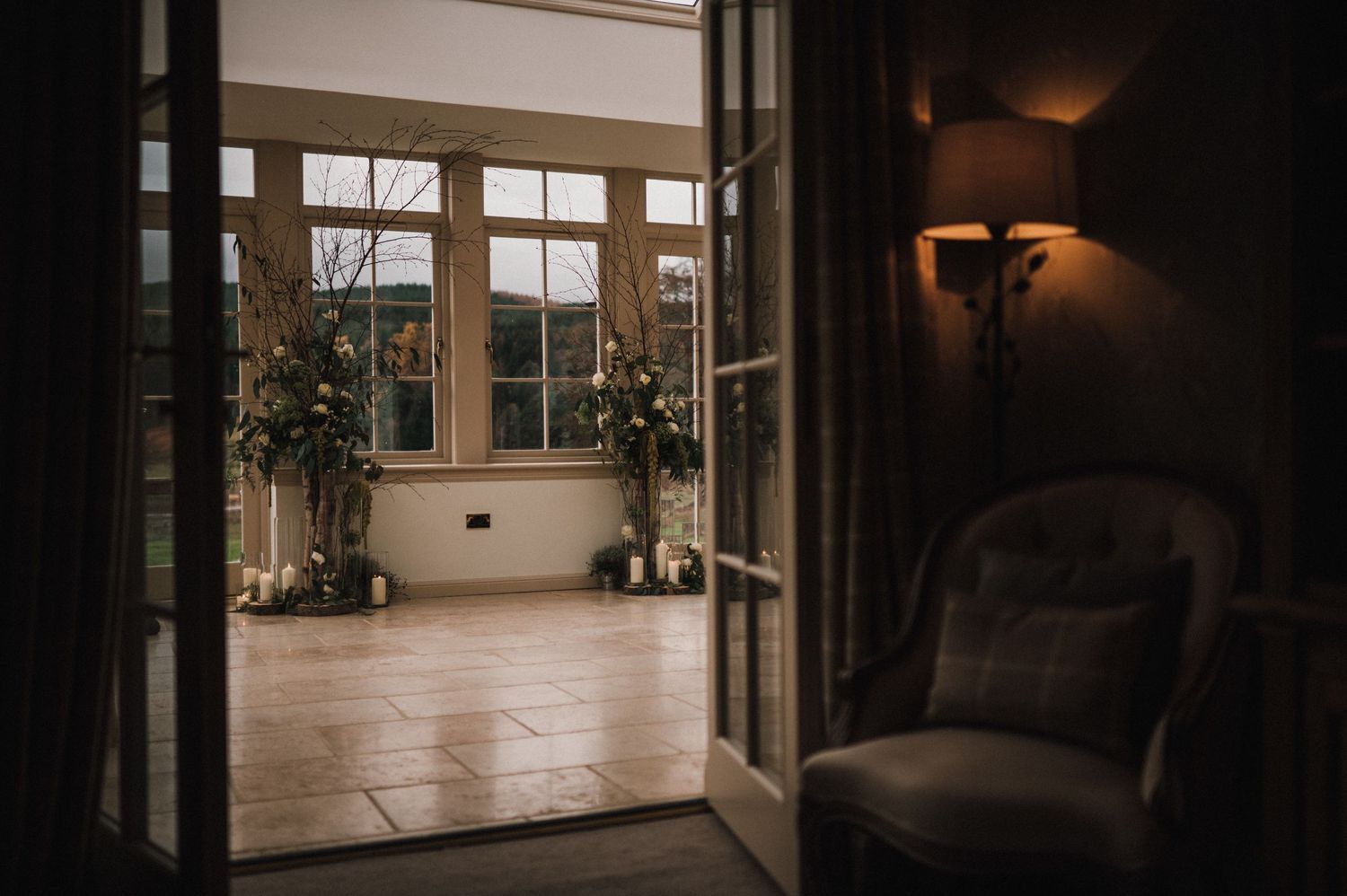 Interior view of elegant room with large windows and armchair showing into sunlit space with plants.
