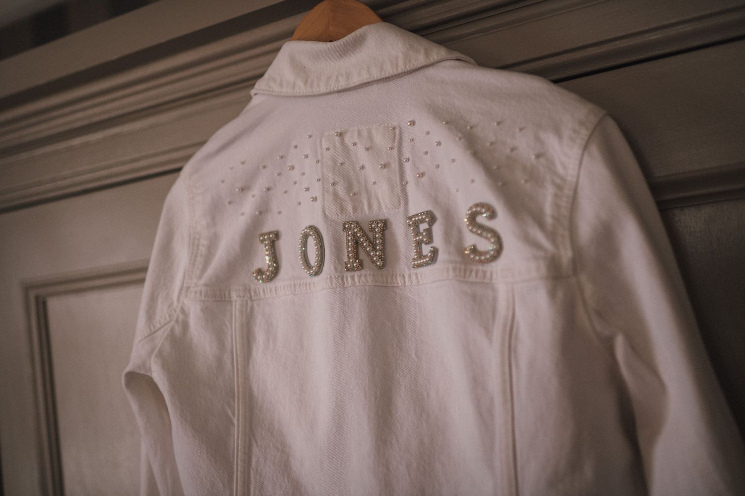 White denim jacket with 'JONES' embroidered on the back hanging on display.