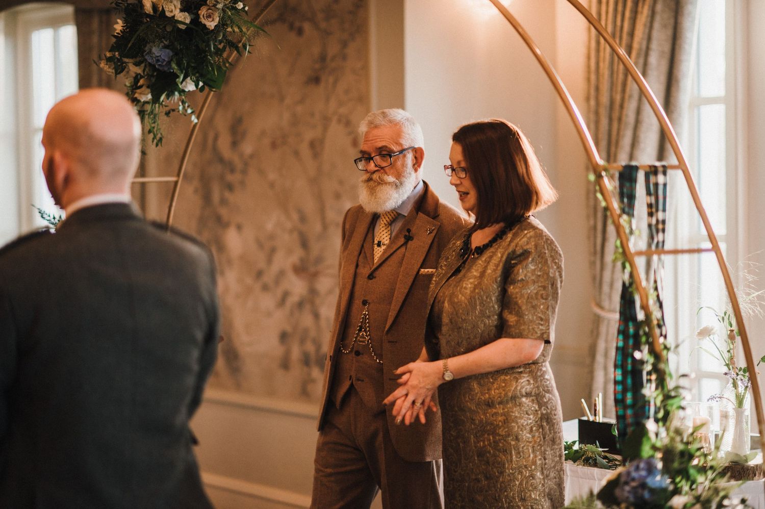 Intimate wedding moment in an elegantly decorated room with vintage wallpaper and natural light.