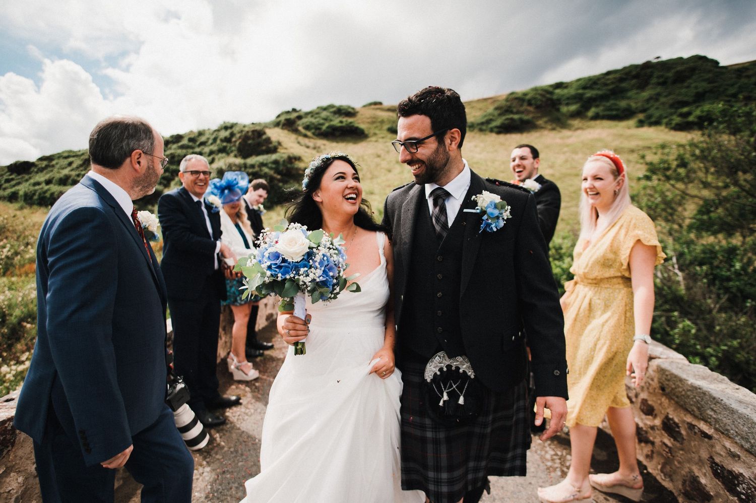 A joyous wedding celebration on a stone bridge pathway with Scottish highlands in the background.