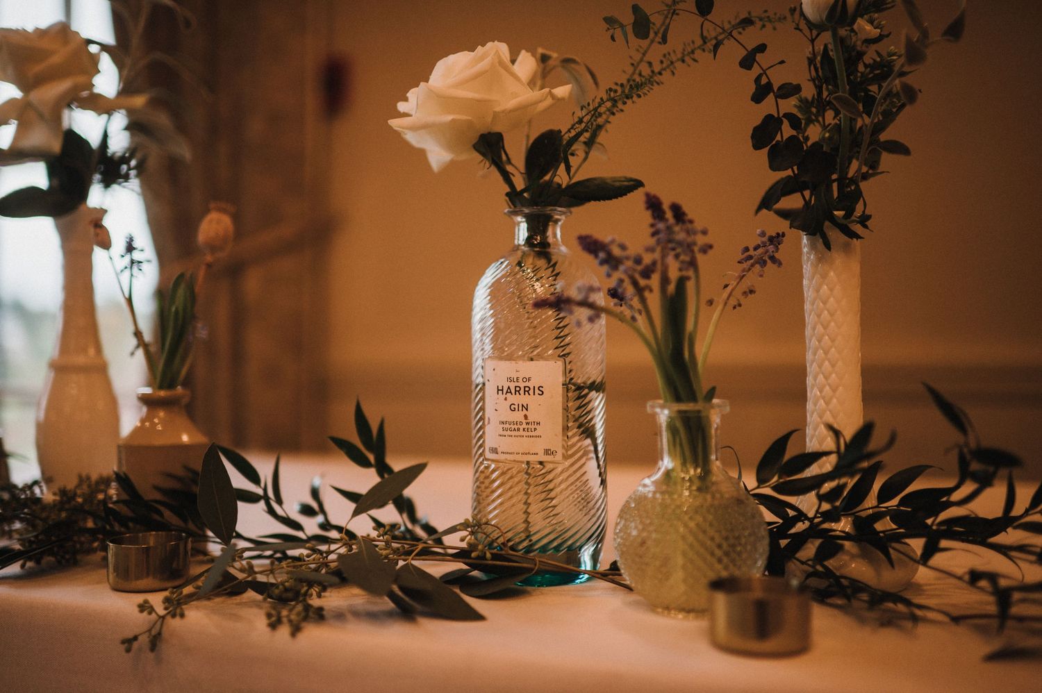 Rustic wedding decor featuring glass bottles with white flowers and greenery on a table.