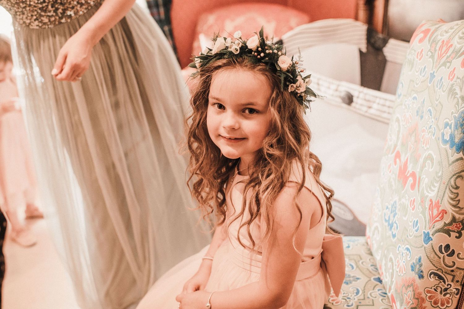 Young attendant wearing a pink dress and floral crown smiles during wedding preparations.