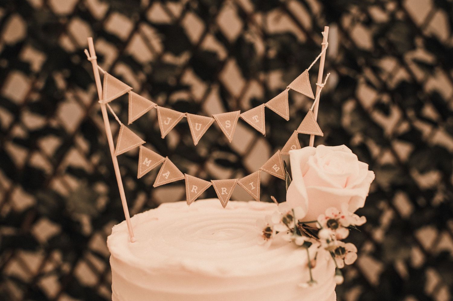 Simple white wedding cake topped with bunting banner and pink rose decoration.