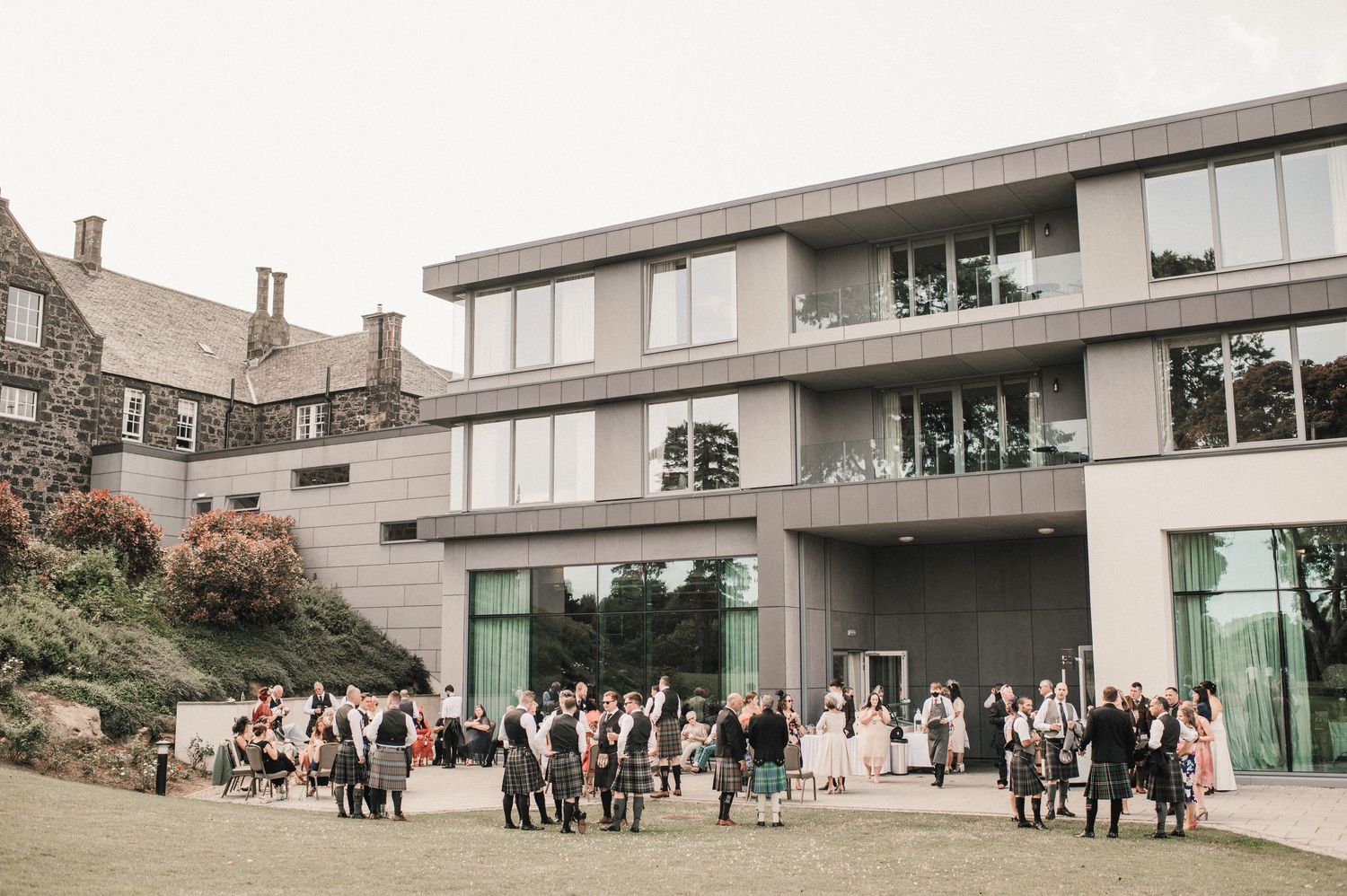 Modern building exterior with wedding guests gathered outside on a sunny day.