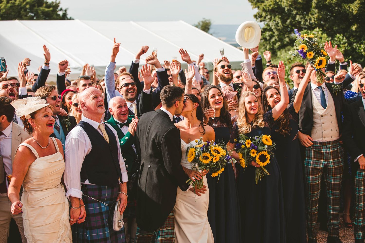 Wedding guests celebrate with raised arms and cheers during outdoor reception.