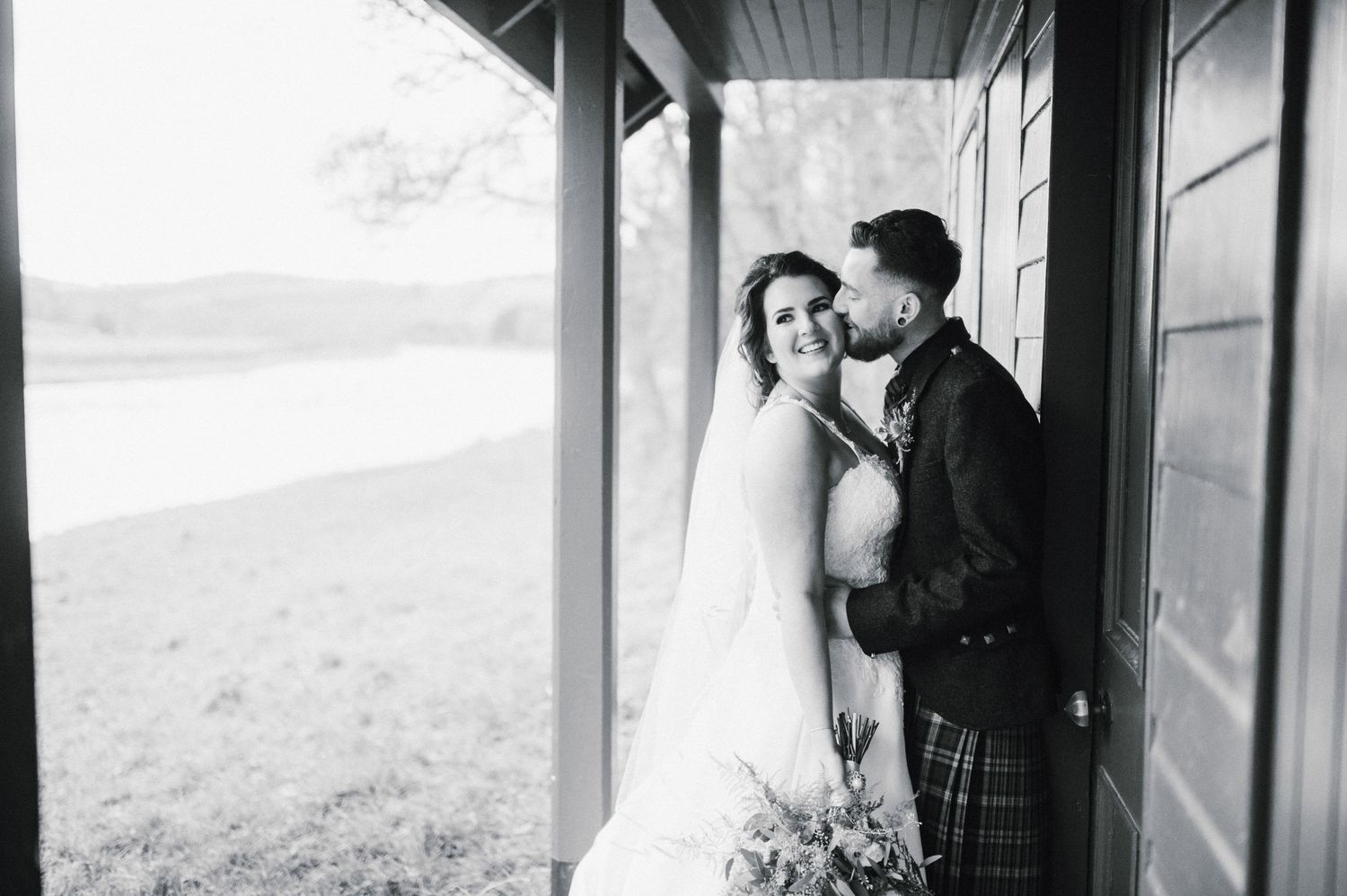 Black and white wedding portrait of couple sharing intimate moment on porch.