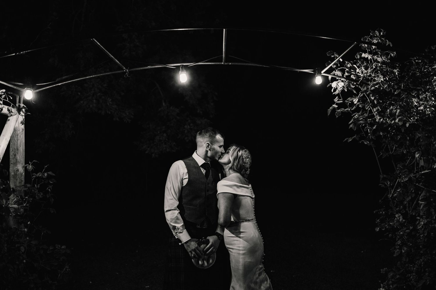 Couples dance under twinkling lights at an outdoor evening celebration.