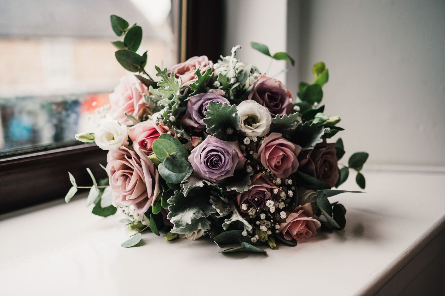 Beautiful wedding bouquet featuring mauve roses and delicate foliage on a light surface.