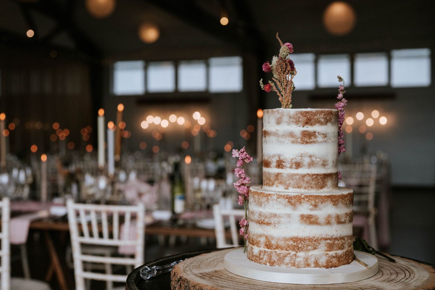 Three-tiered naked wedding cake decorated with fresh flowers on display.