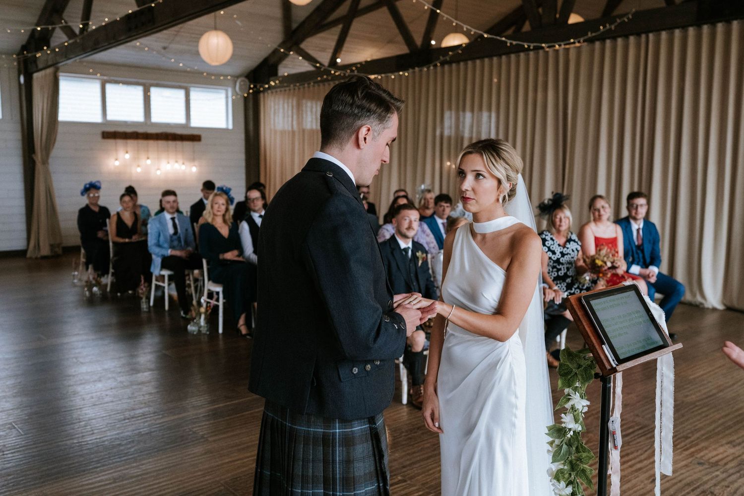 Wedding ceremony taking place in rustic venue with exposed beams and wooden floors.