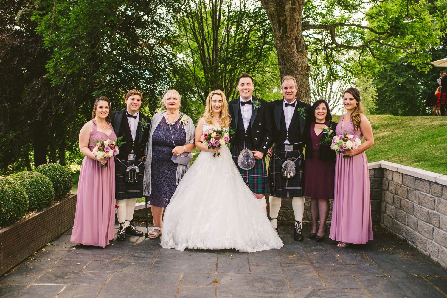 Wedding party in pink bridesmaid dresses and formal attire posing outdoors.
