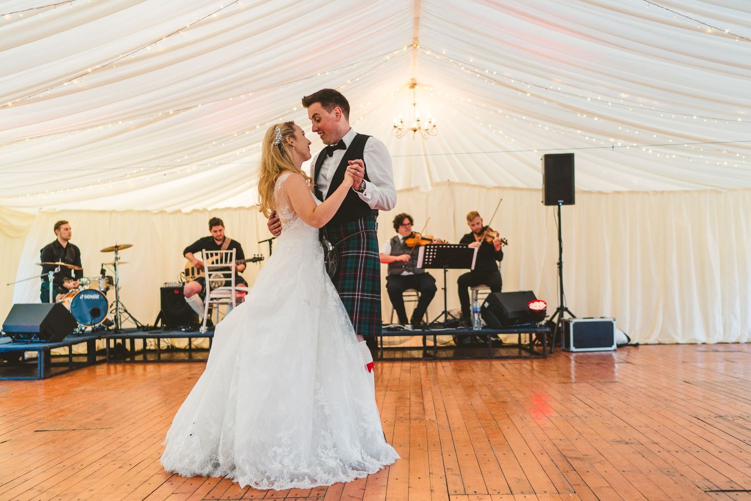 Wedding reception dance floor in a white marquee tent with band setup visible.