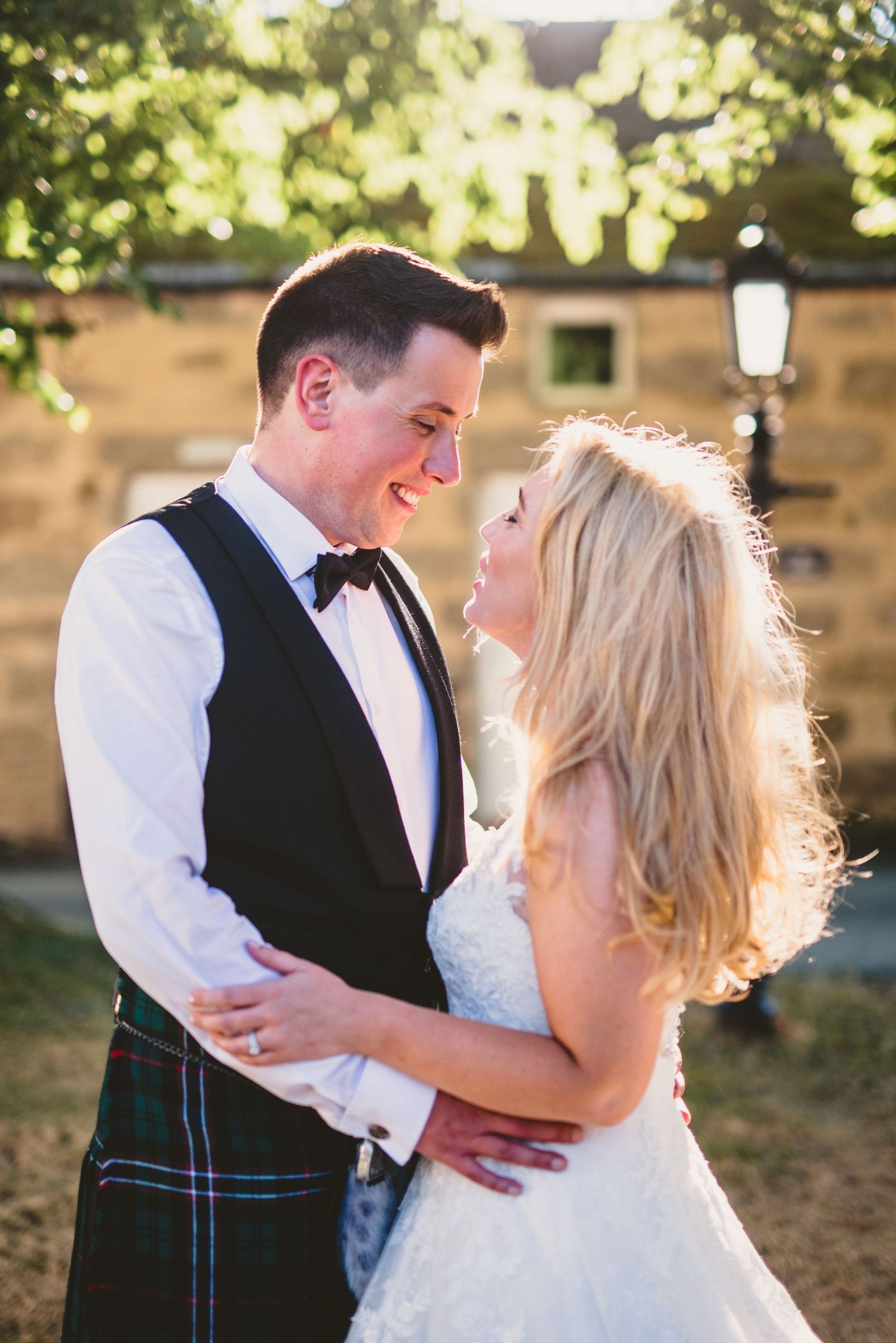 A couple embraces in romantic sunlit moments during their wedding celebration outdoors.