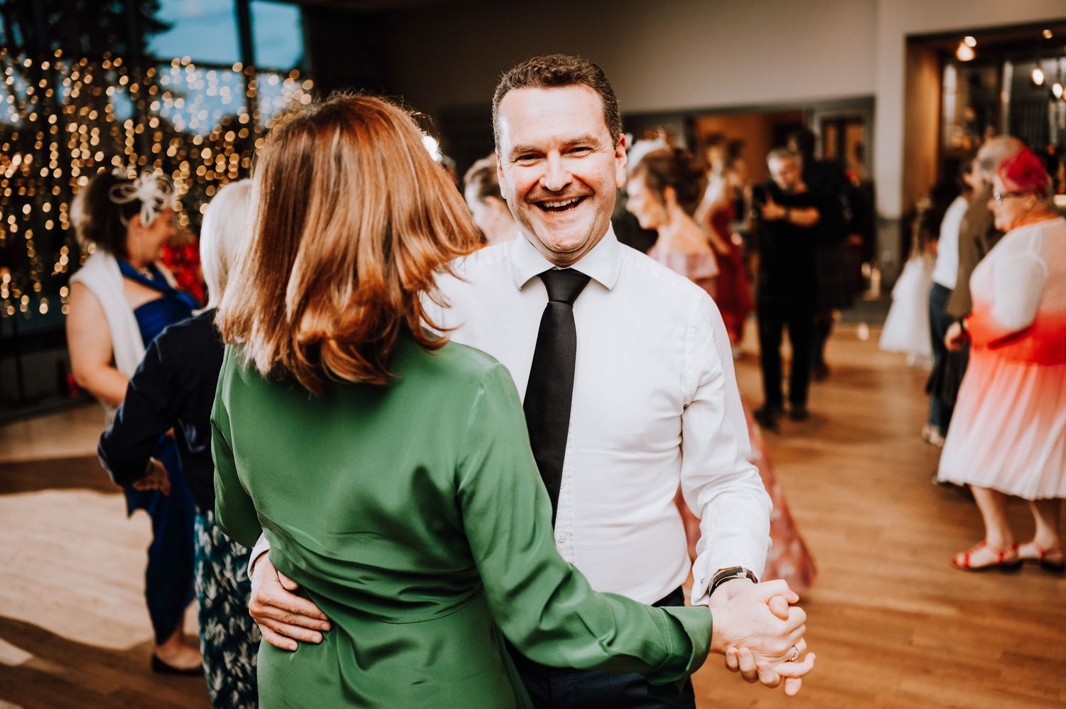 Wedding guests dancing and celebrating in an indoor venue with festive lighting. Meldrum House Wedding Photography.