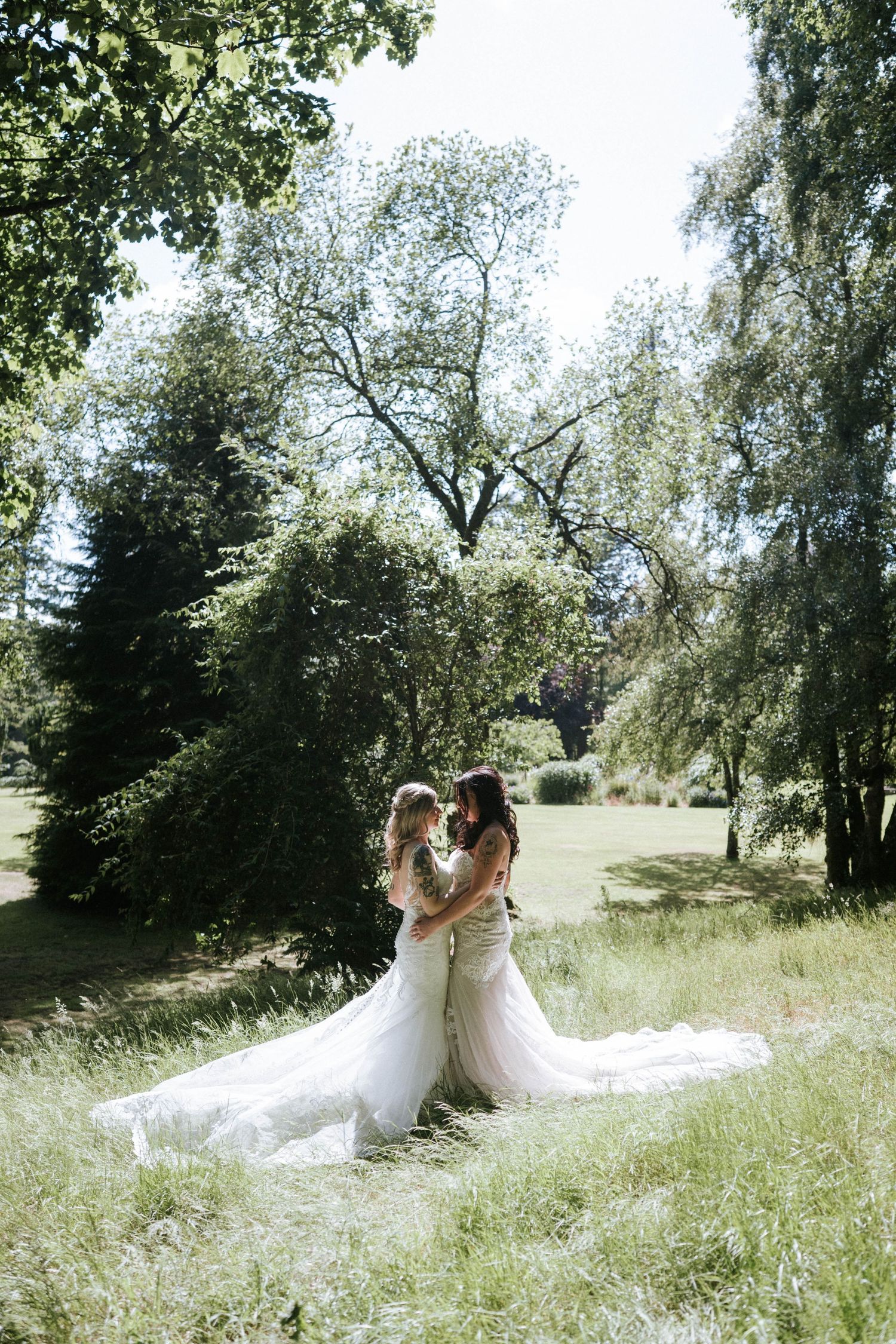 Fasque Castle Wedding Photography. Wedding couple embraces on grassy hillside surrounded by trees on sunny day.