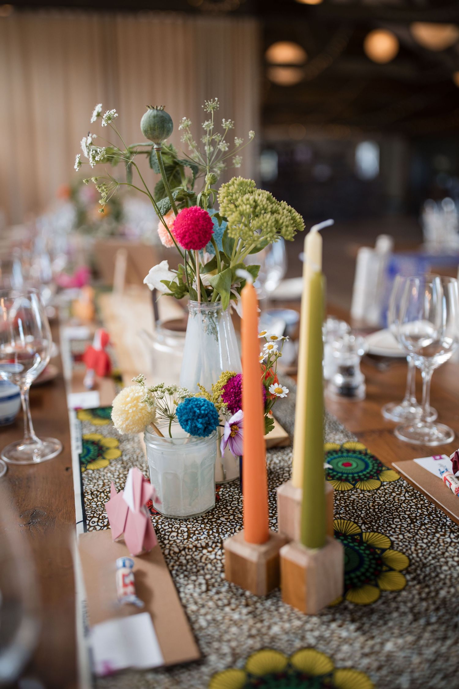 Colorful candles and delicate floral centerpieces line a rustic wedding reception table with polka dot runners.