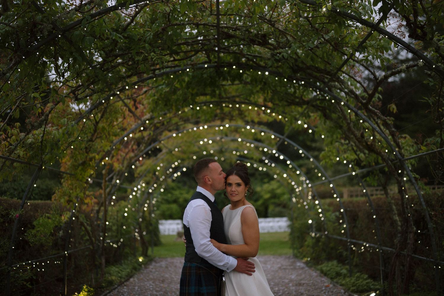 Romantic garden pathway with twinkling lights strung through tree branches overhead.