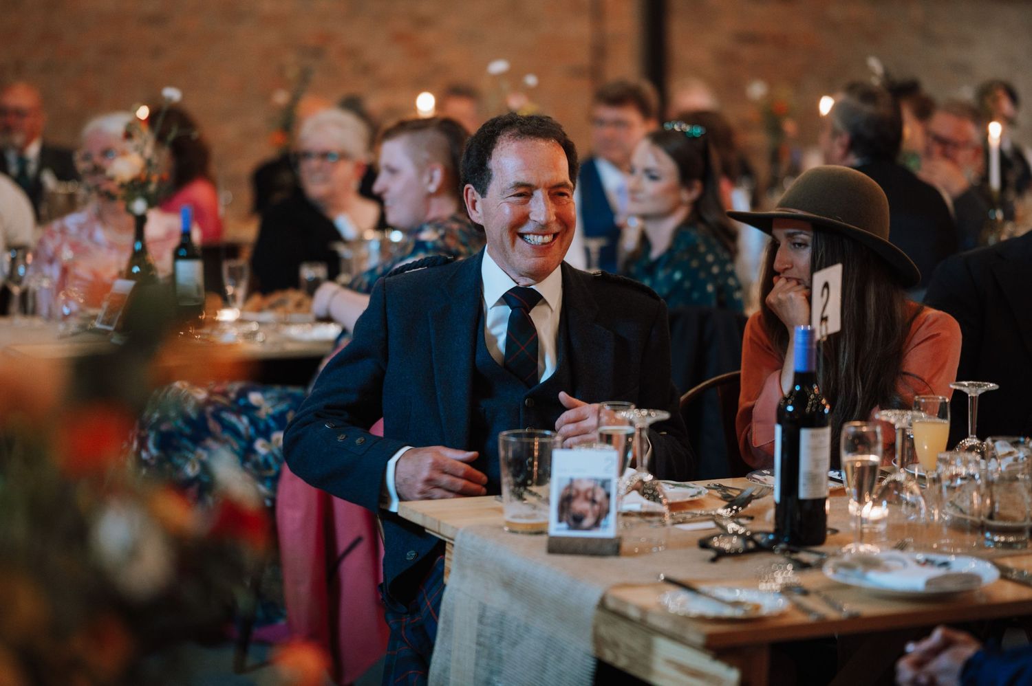 Wedding reception guests enjoy dinner and conversation at rustic venue.