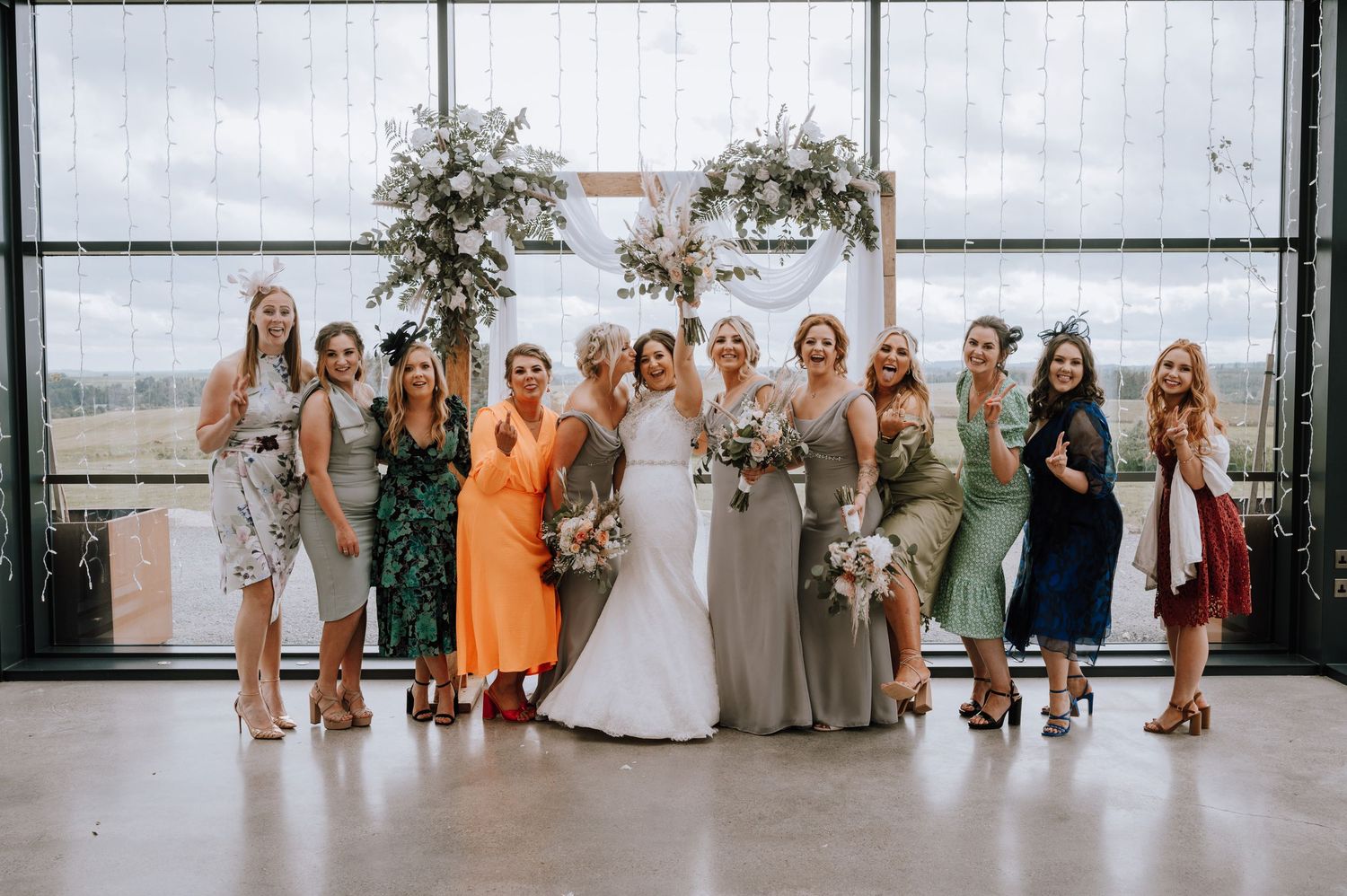 Wedding party poses together in front of large windows at a modern venue.