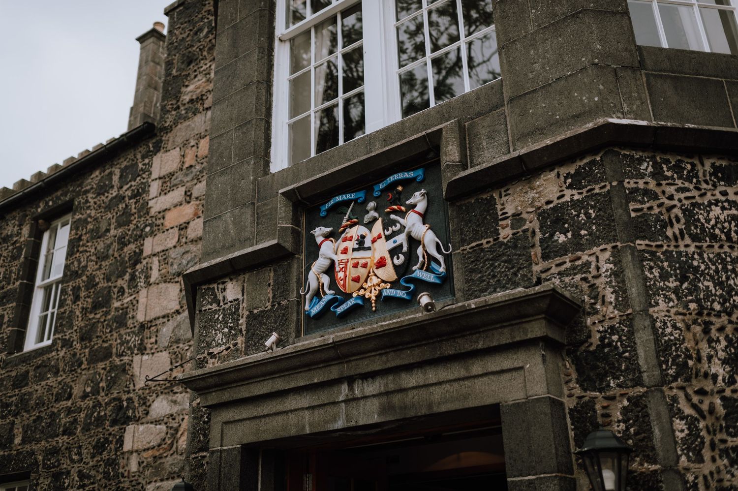 Decorative heraldic crest mounted on stone wall of historic building.