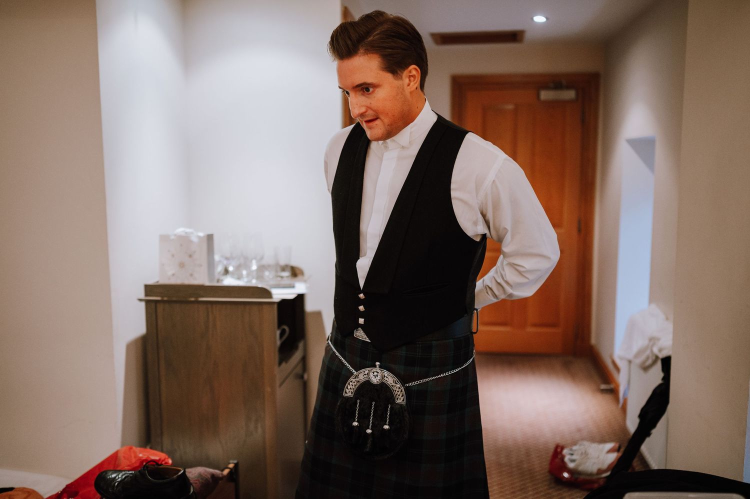 Man wearing traditional Scottish formal attire with sporran in hotel room.
