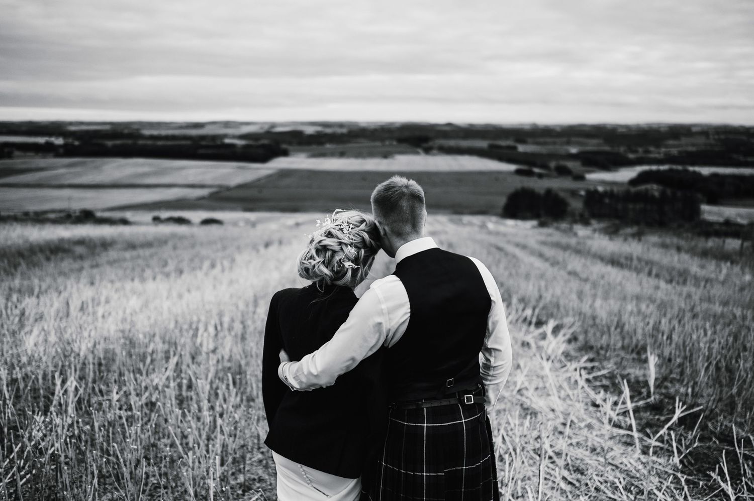 Black and white photo of a couple in traditional Scottish dress overlooking rolling hills during their wedding.
