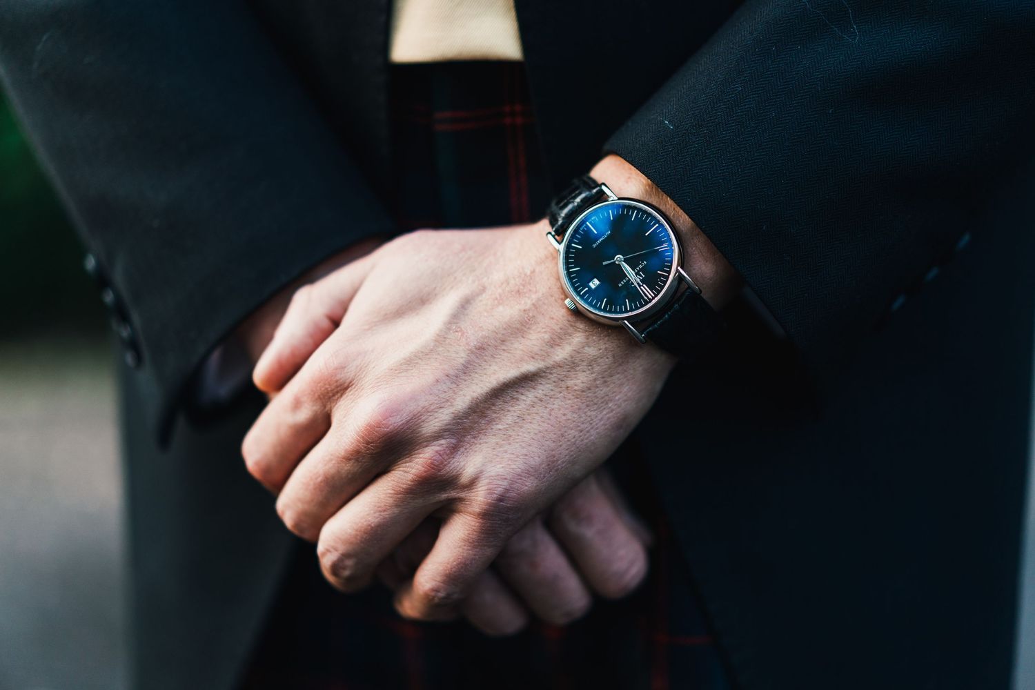 Close-up shot of a wrist wearing an elegant blue-faced watch with a leather strap against a dark background.