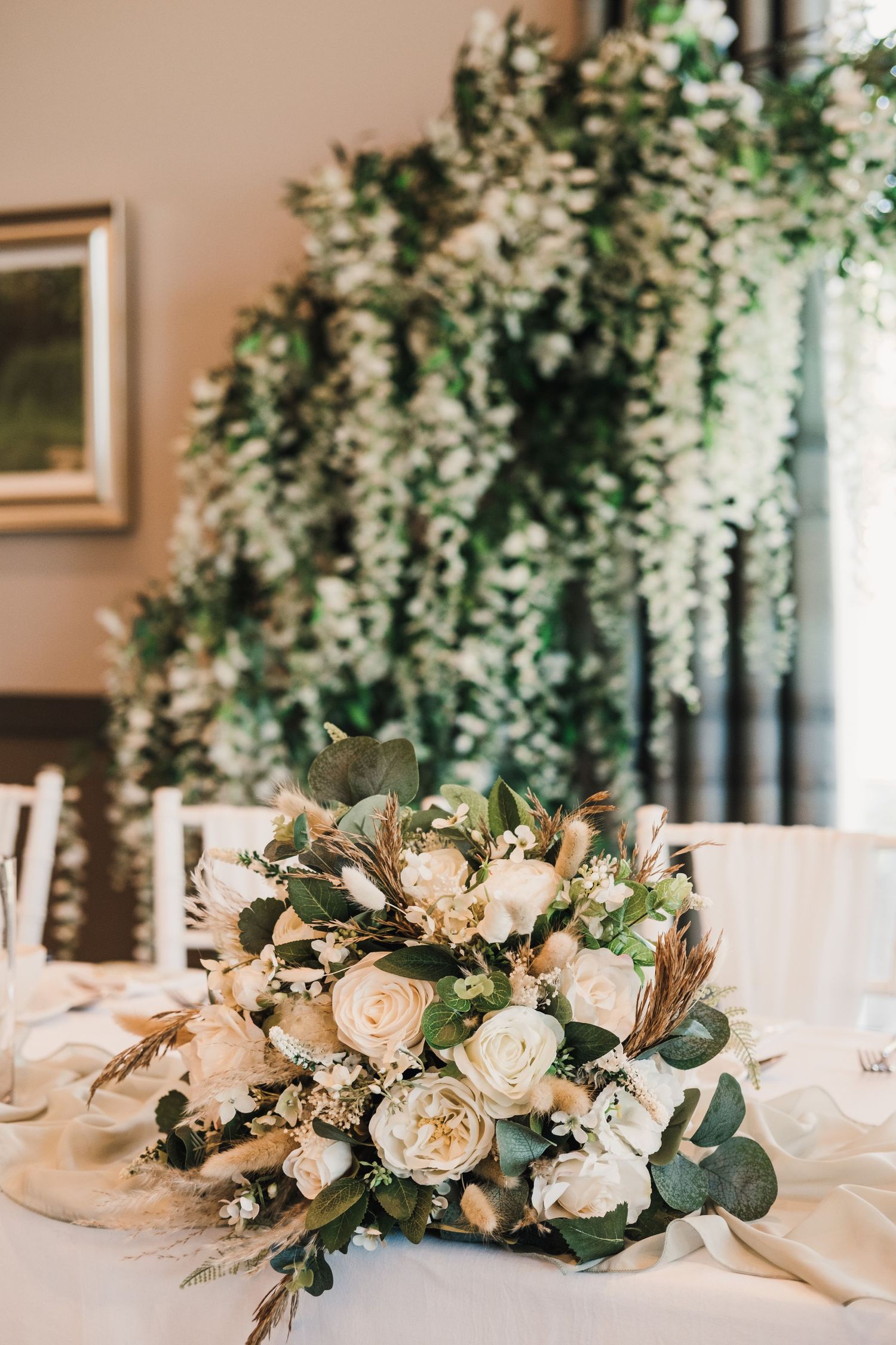 Beautiful white rose and eucalyptus centerpiece arrangement on a wedding table with cascading wisteria in background.