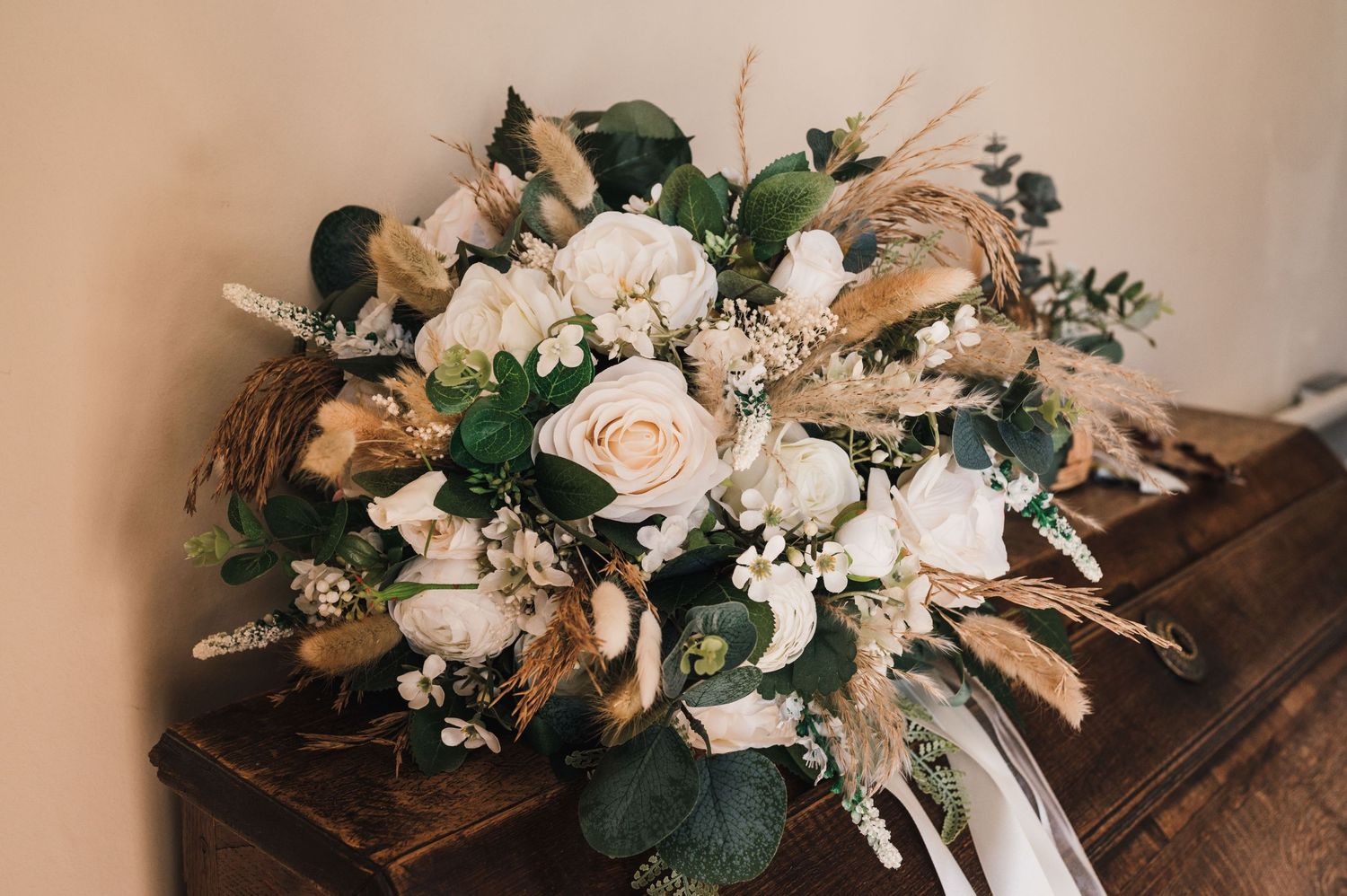 Elegant wedding bouquet with blush roses, white flowers, and dried elements displayed on wooden surface.