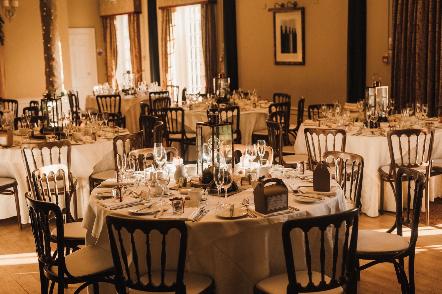 An elegant wedding reception setup with round tables, white linens and classic chairs in a warm-lit room.