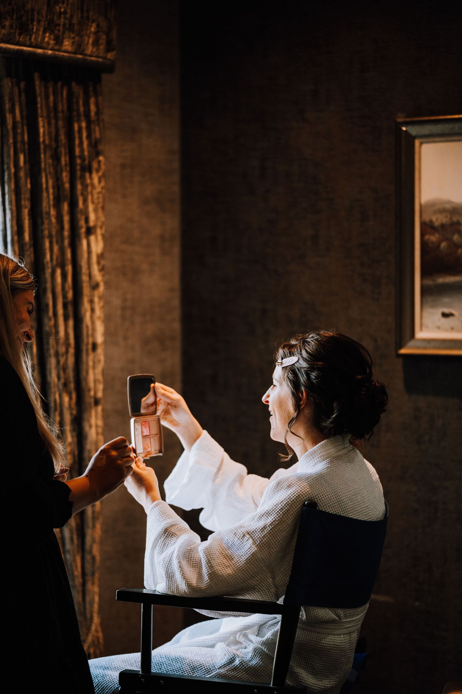 Person in white robe holding up a small bottle in dramatic window lighting.