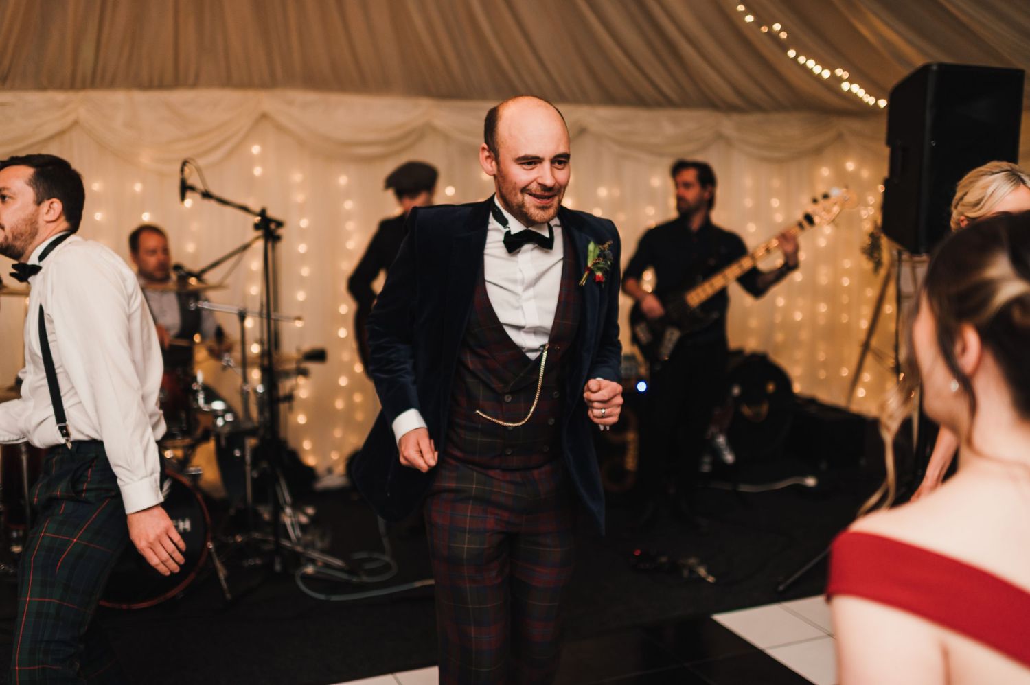 Wedding reception features live band performing while guests dance under draped fabric and string lights.
