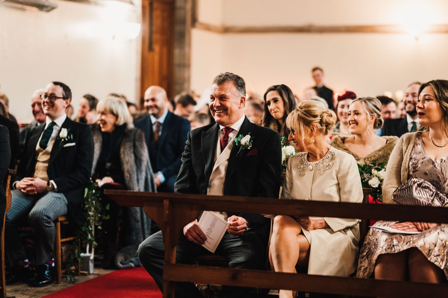 Wedding guests smile and enjoy the ceremony from wooden church pews.