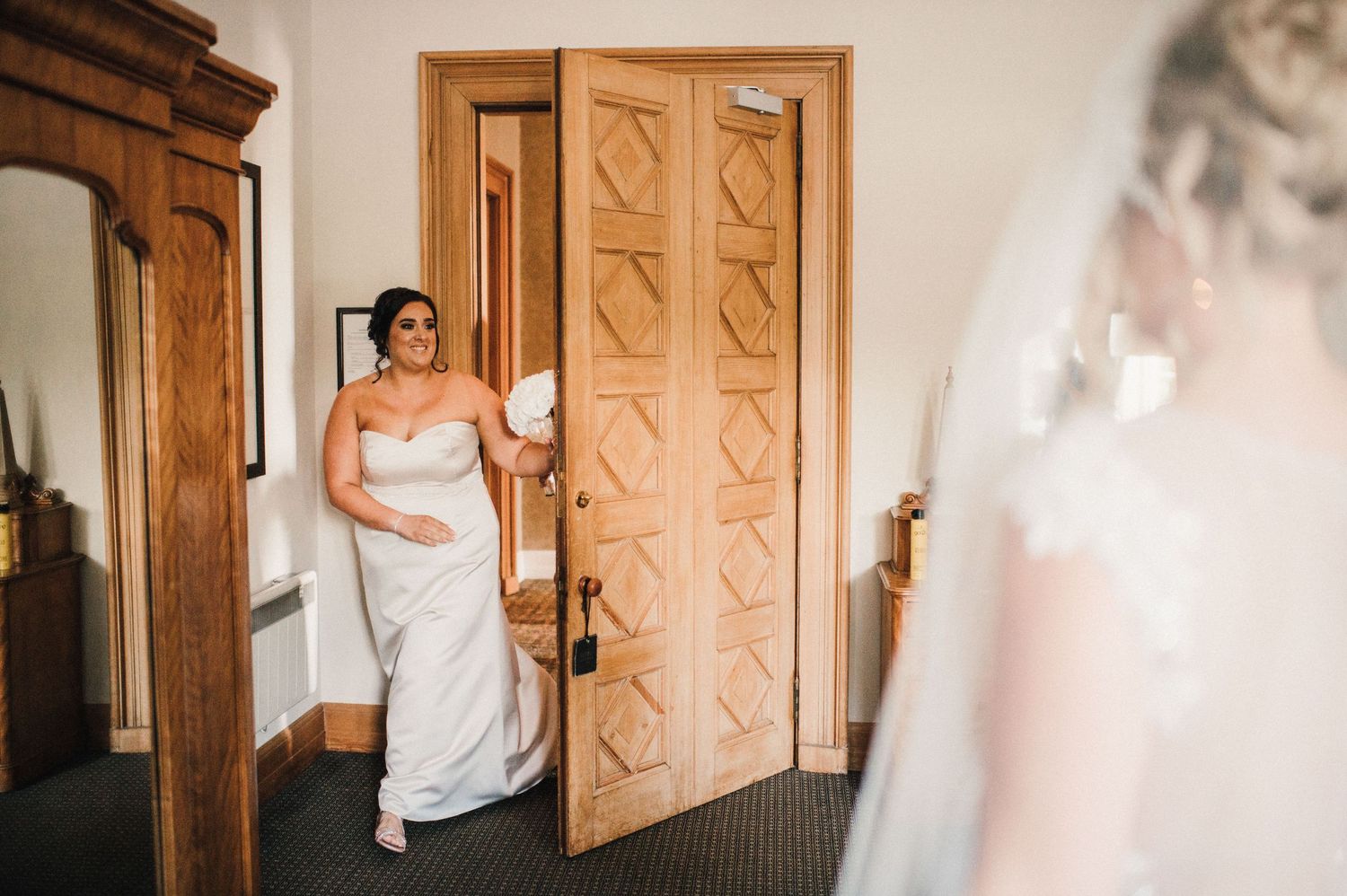 A bride in white gown stands in doorway of elegant room with wooden details.