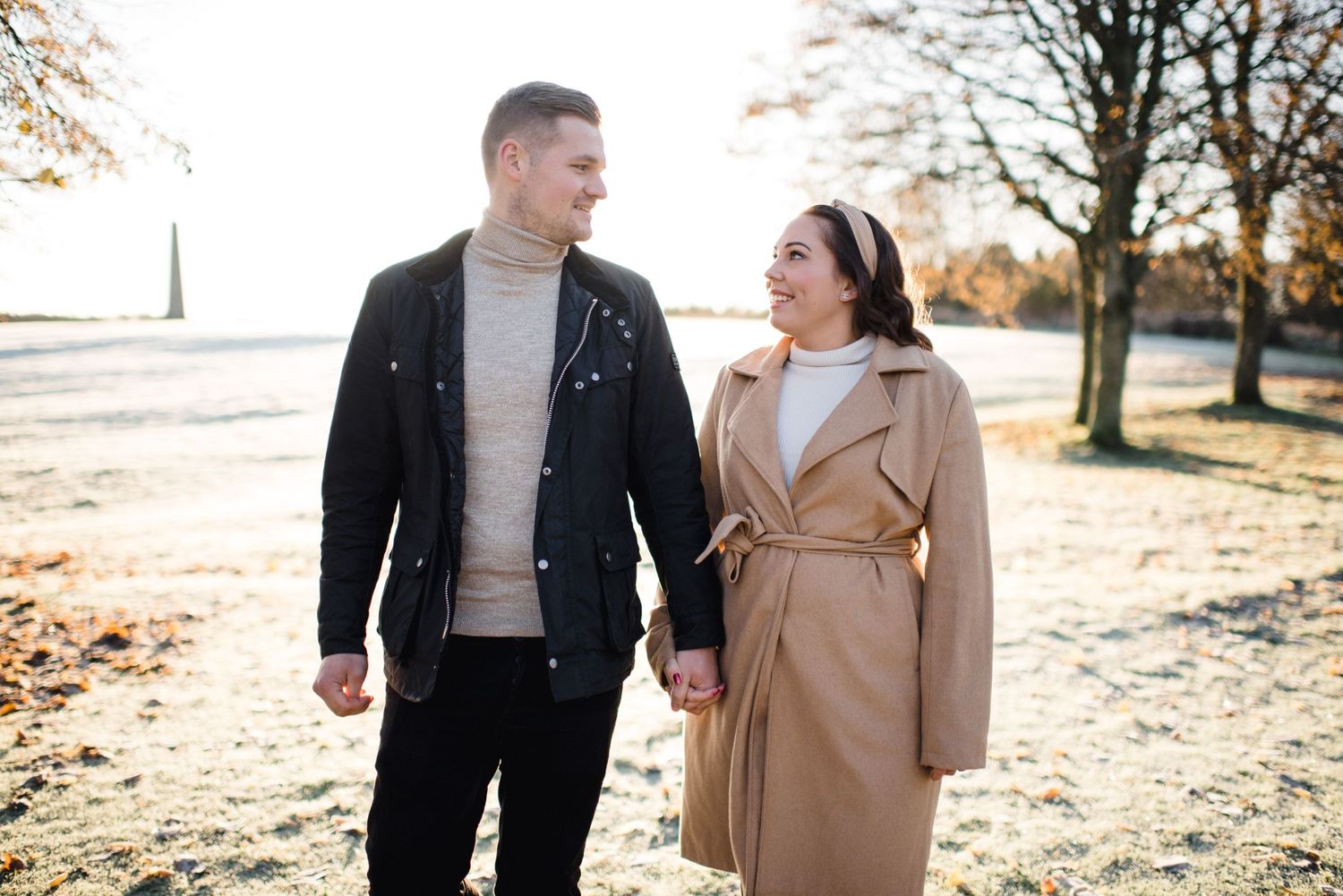 Couple enjoying autumn stroll through park in matching winter coats.