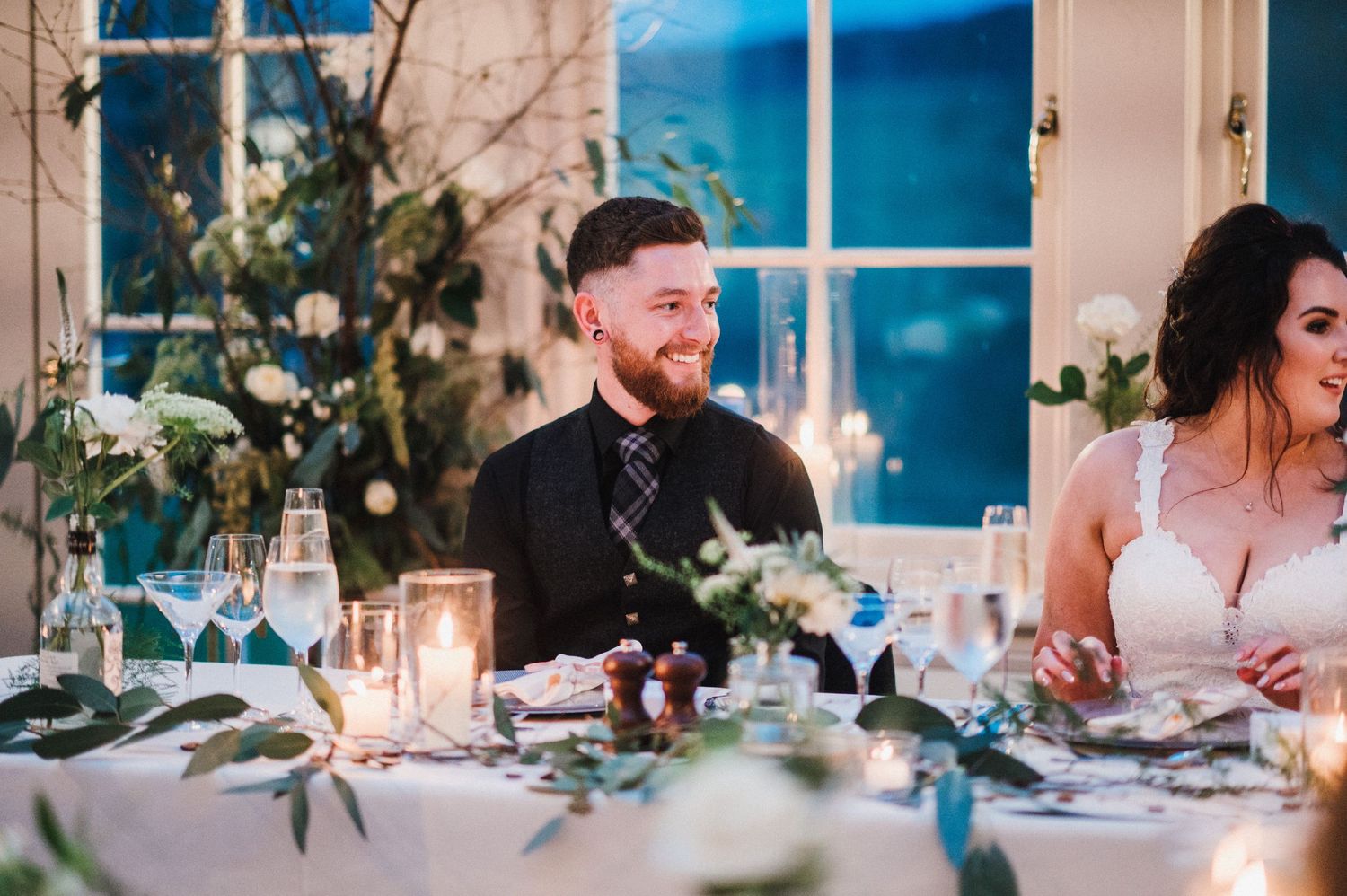 Wedding reception dinner table with candlelight and greenery decorations.