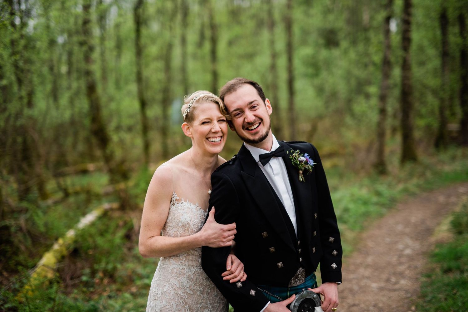 A couple shares a joyful moment together on a wooded forest path during their wedding celebration.