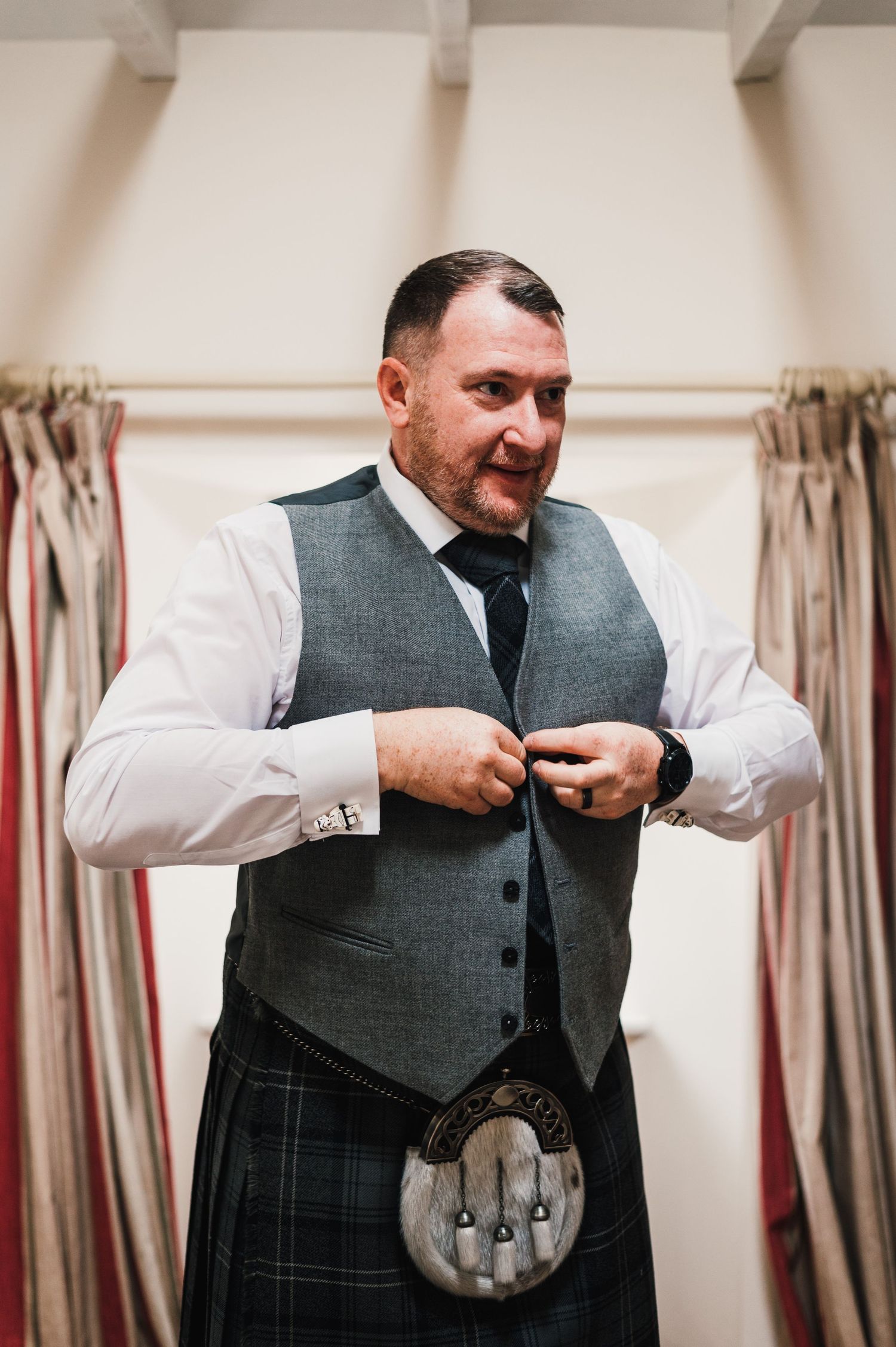 A person wearing a grey vest and white shirt adjusts their outfit while getting ready for a formal event.