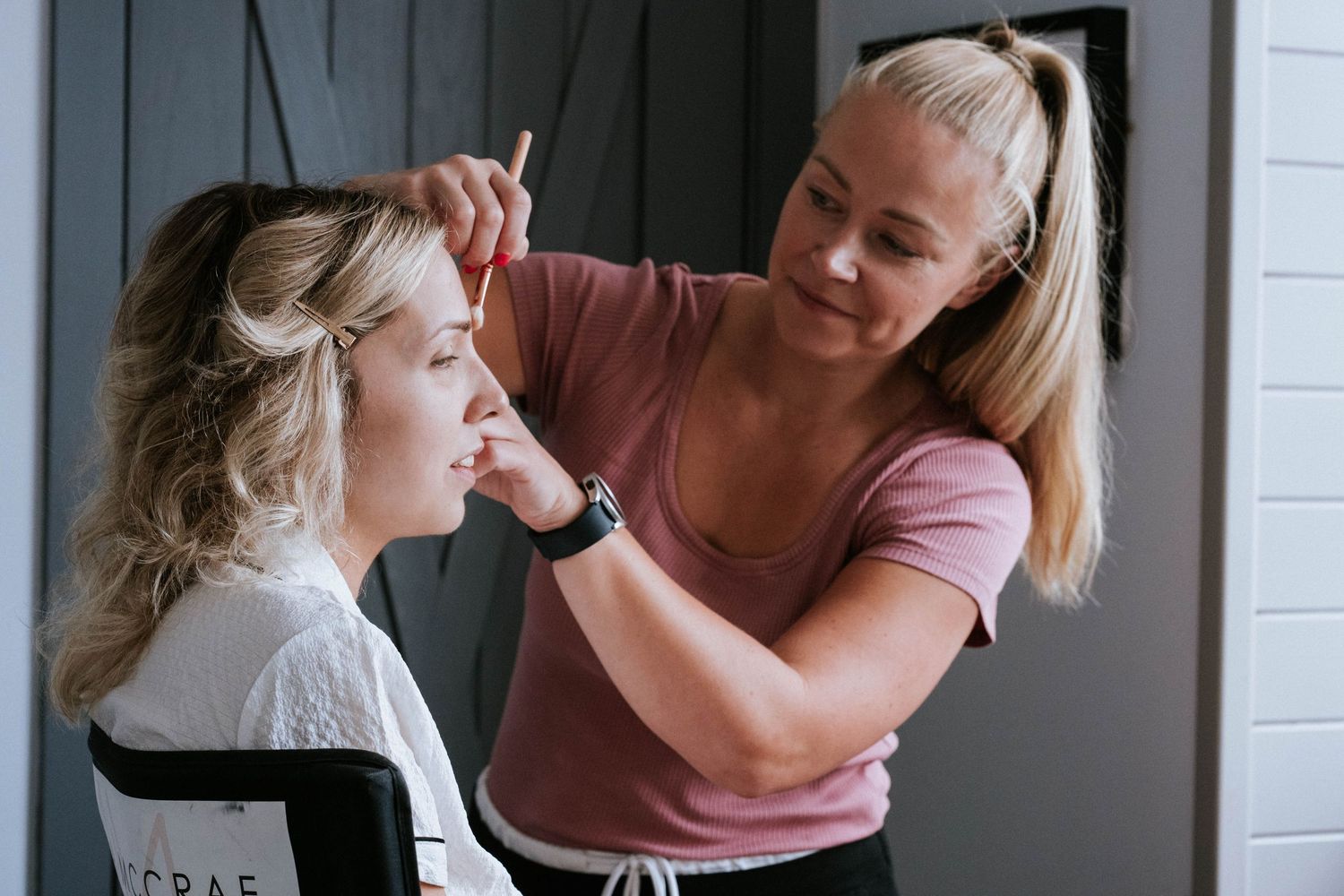 A makeup artist applies cosmetics to a client sitting in a chair during a professional beauty session.