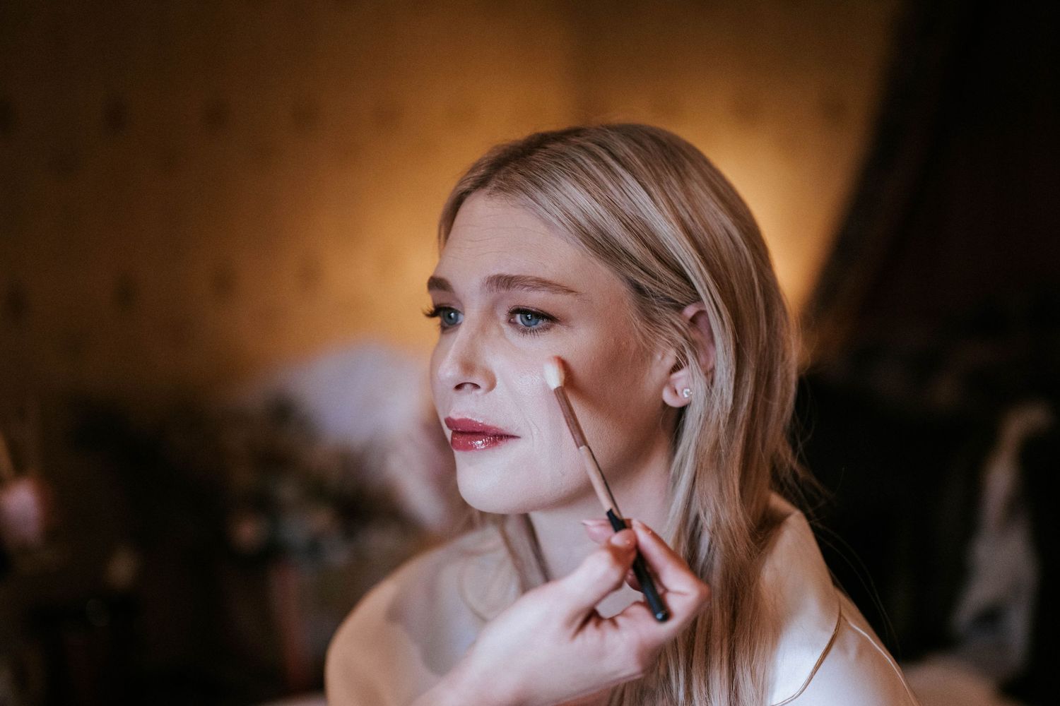 Someone having makeup applied while sitting in a chair during a beauty preparation session.