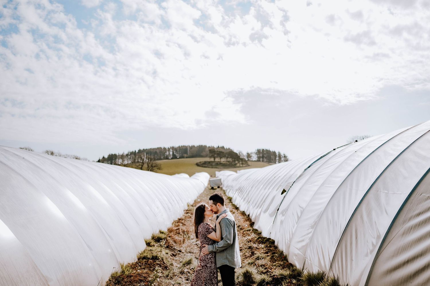 Engagement photography session Aberdeen. A series of white polytunnels stretch across a farm field under cloudy skies.