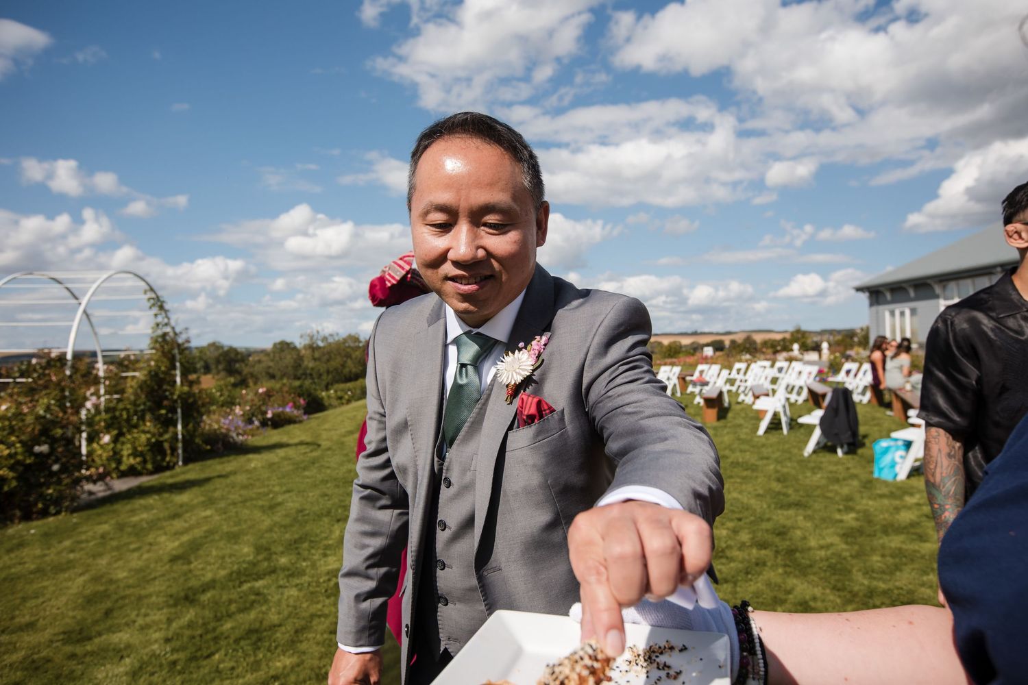 Wedding party gathering outdoors under blue sky with white clouds.