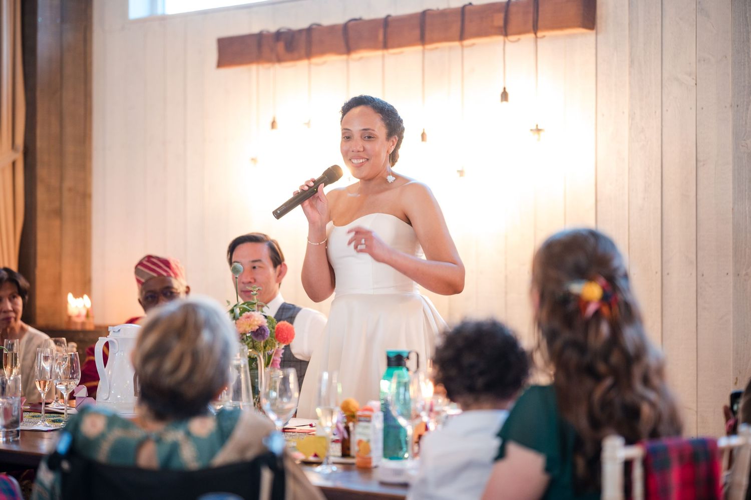 Wedding reception venue with string lights and guests seated at long banquet tables.