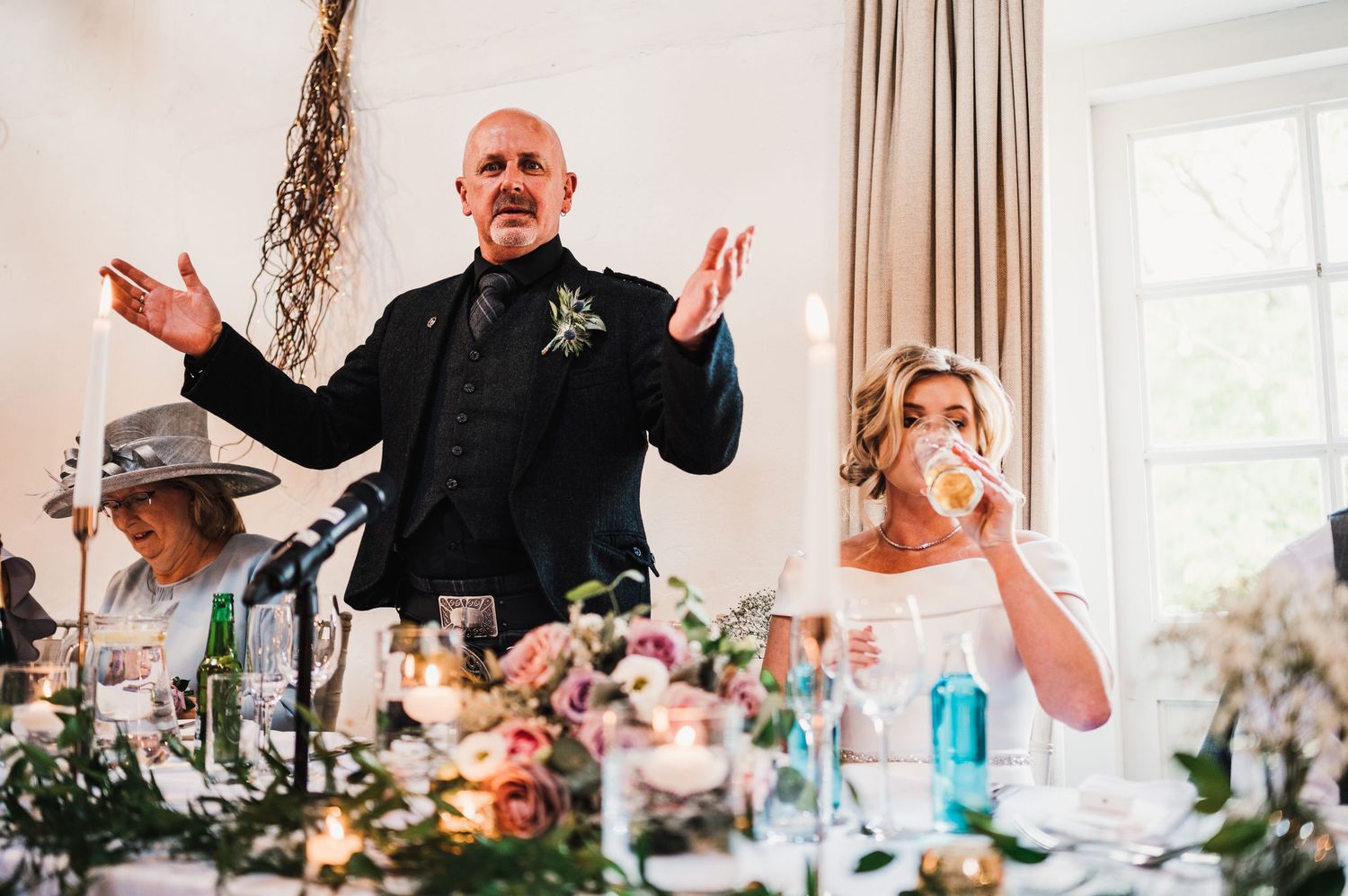 Candid moment during wedding speeches at an elegant reception with floral table decorations.