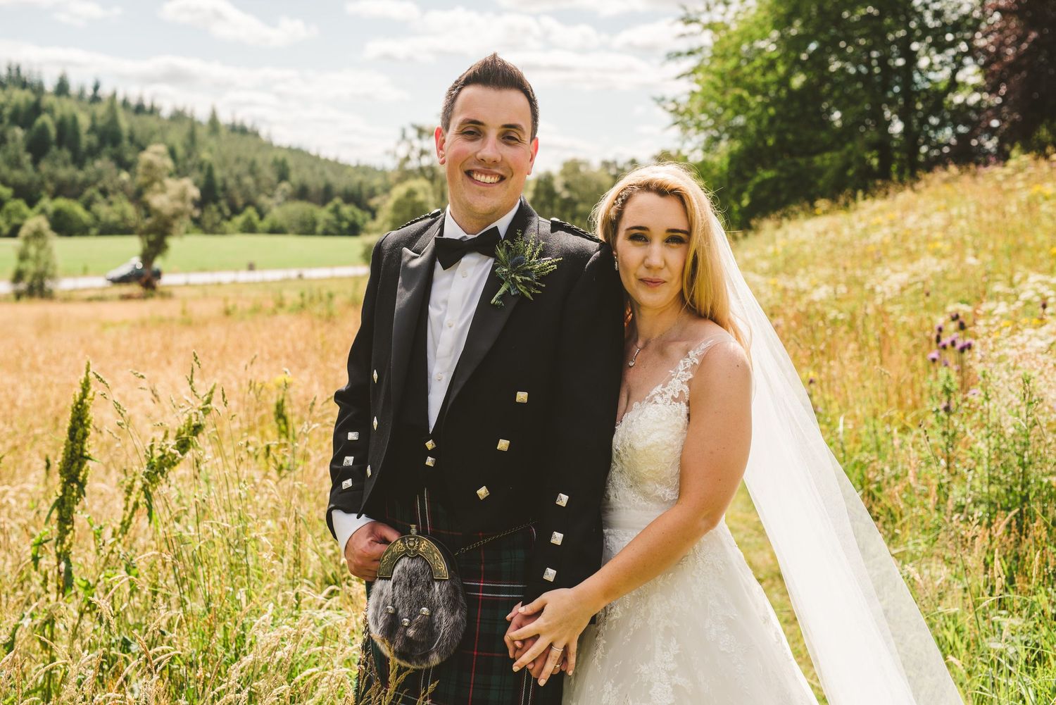 Couple poses together in a scenic meadow with mountains in the background.