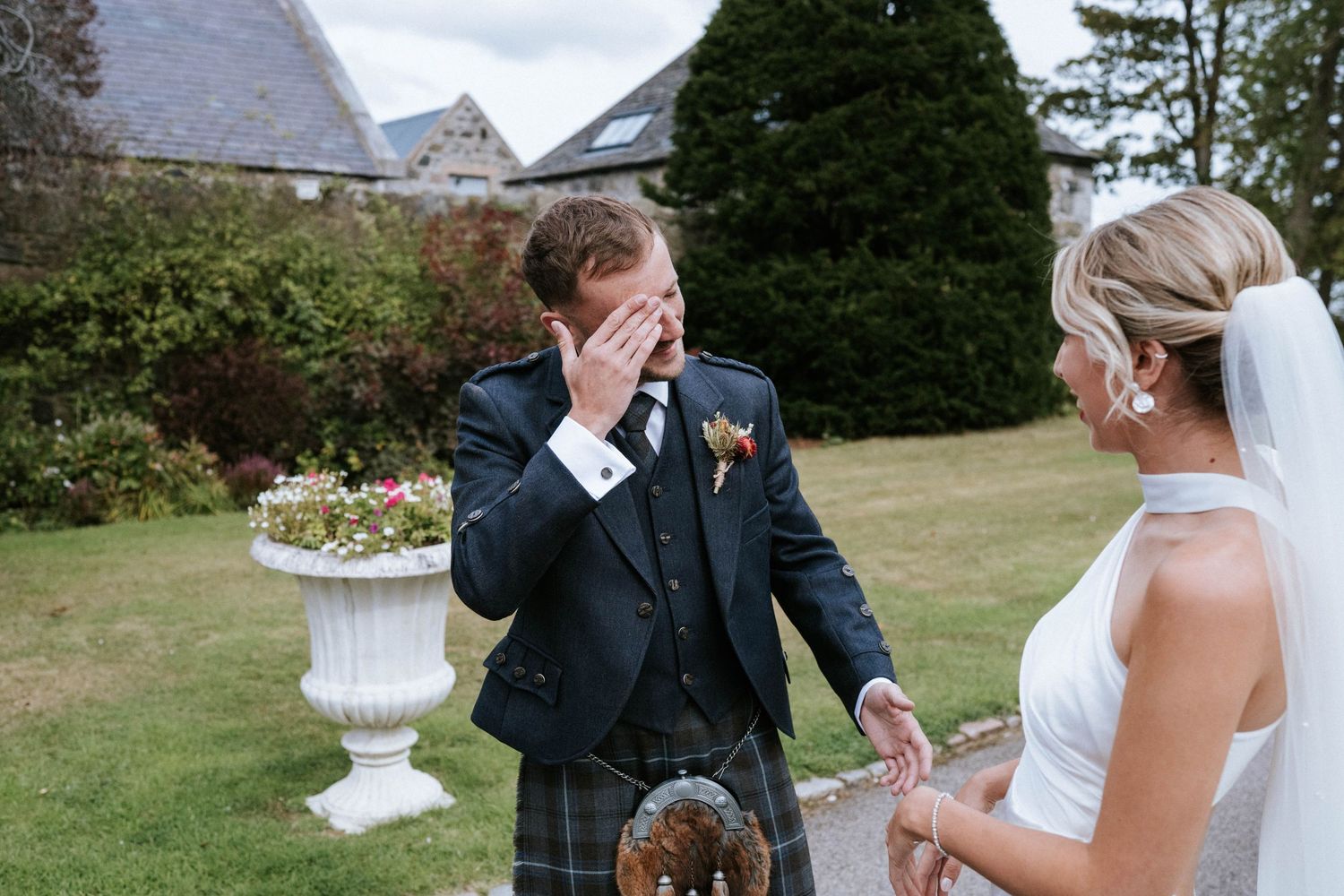Emotional wedding moment captured in garden setting with traditional Scottish attire.