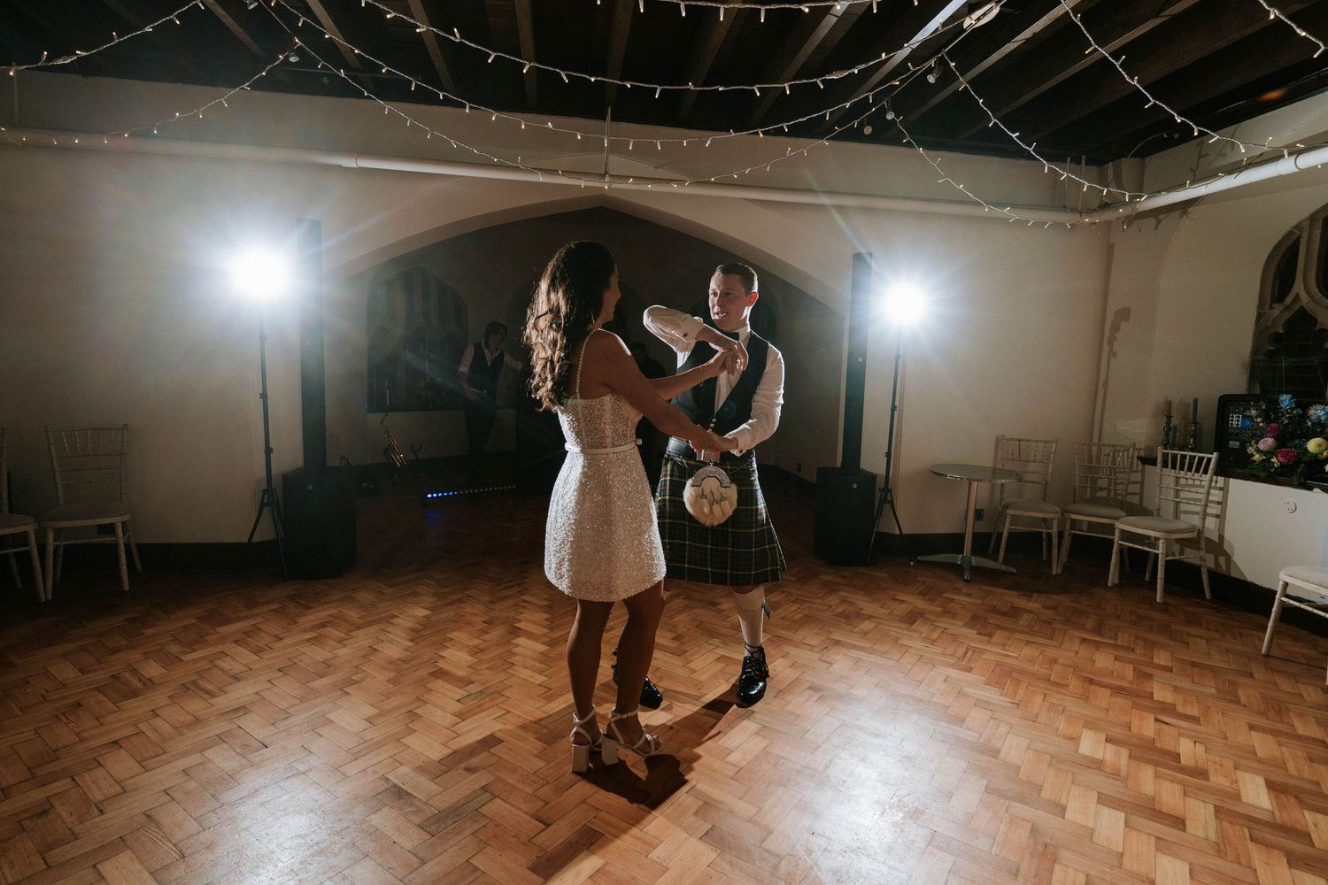 Couples dancing at a wedding reception under twinkling ceiling lights on a wooden dance floor.
