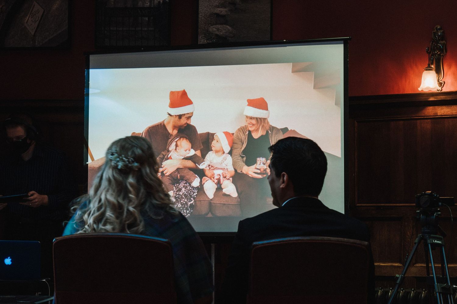 Audience members watch a festive holiday-themed projection in a darkened theater.